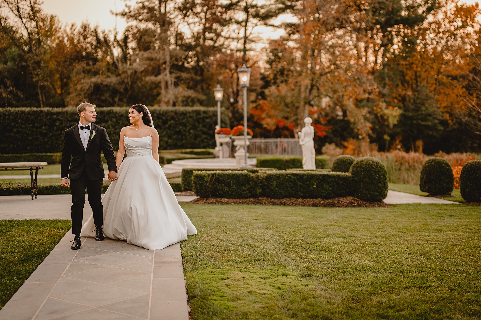 bride and groom hold hands walking through gardens of Park Chateau Estate 