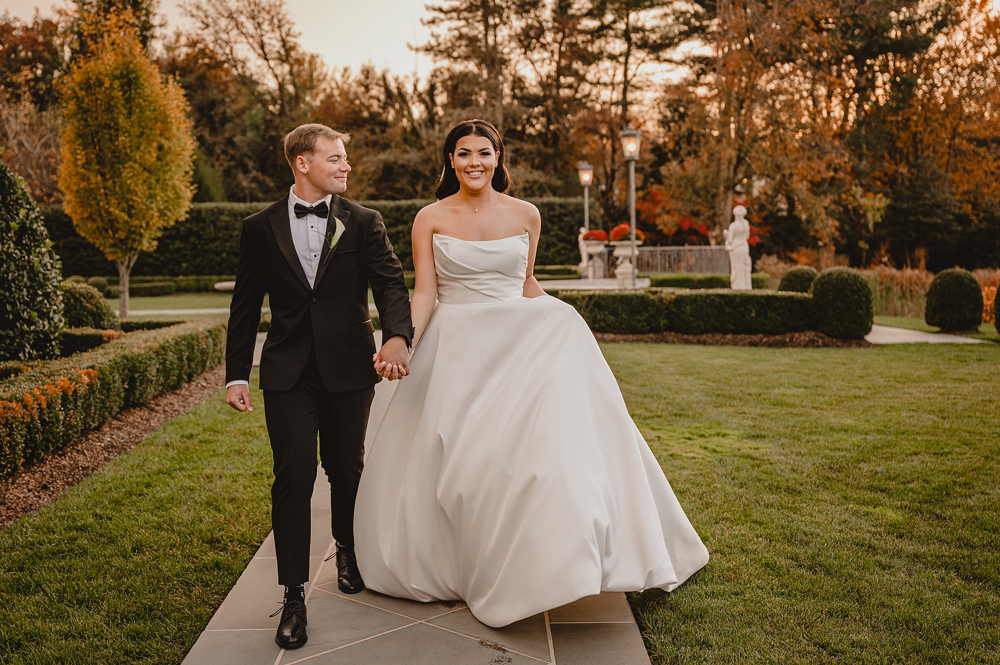 newlyweds hold hands walking down path in garden of Park Chateau