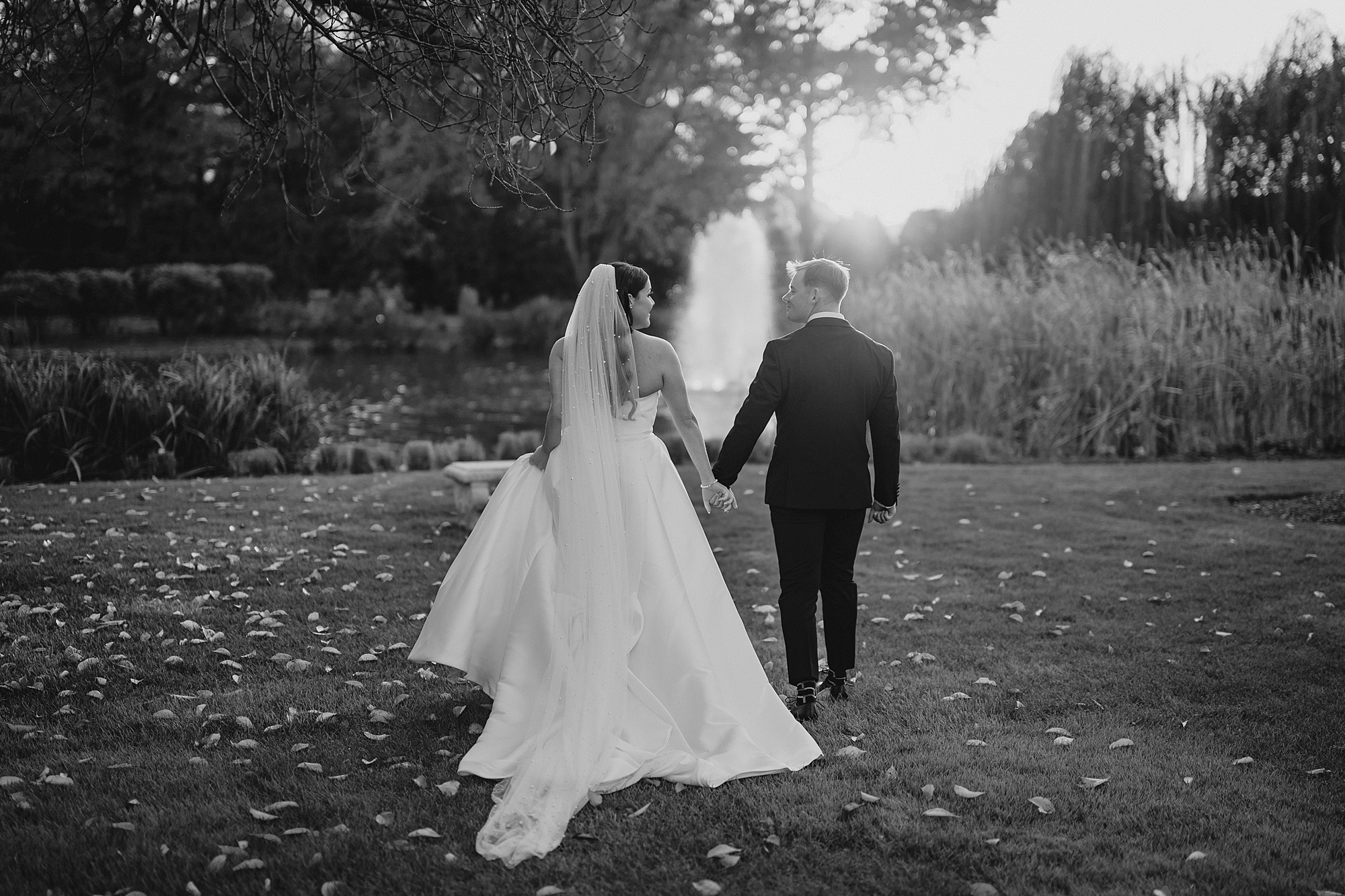 bride and groom hold hands walking towards fountain