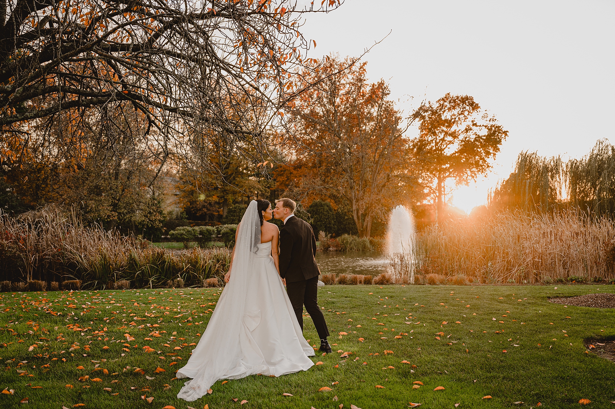 groom leans to kiss bride's cheek in front of fountain at Park Chateau
