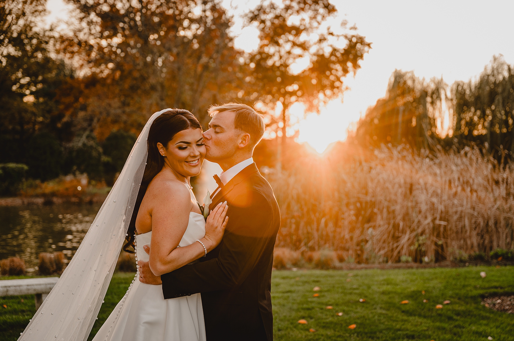 groom hugs bride to him kissing her forehead at sunset during wedding photos at Park Chateau