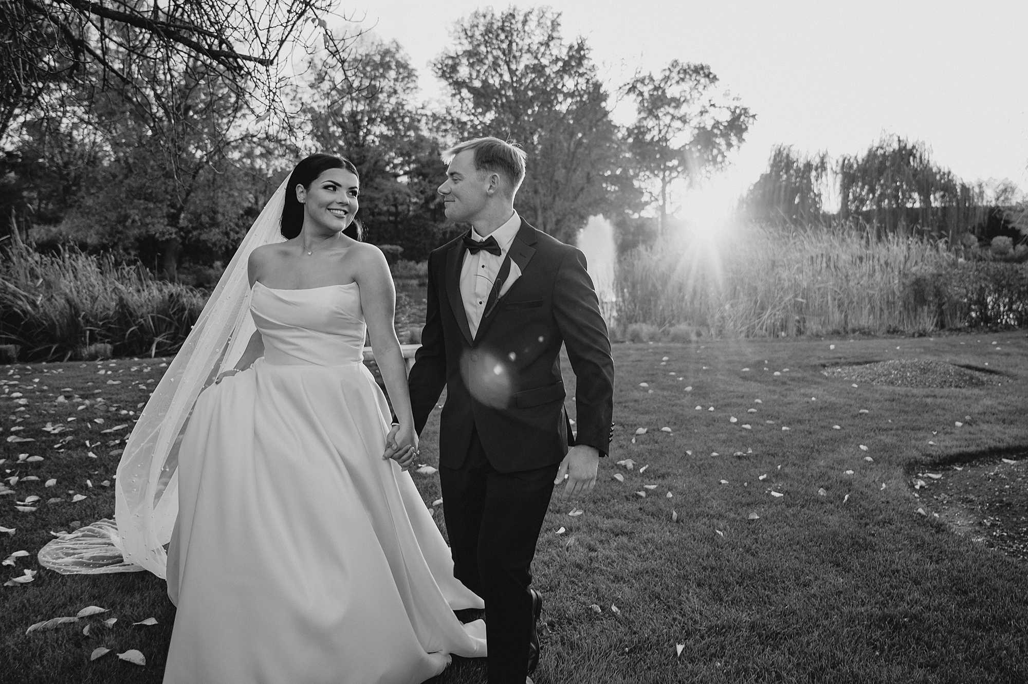 bride and groom hold hands walking through yard near fountain 