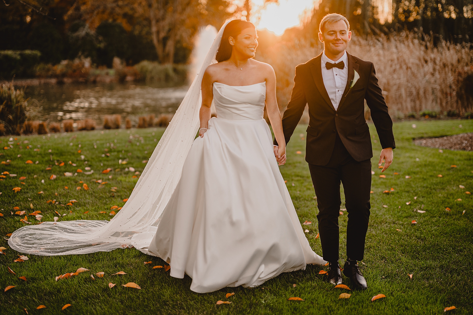newlyweds hold hands walking away from pond at Park Chateau