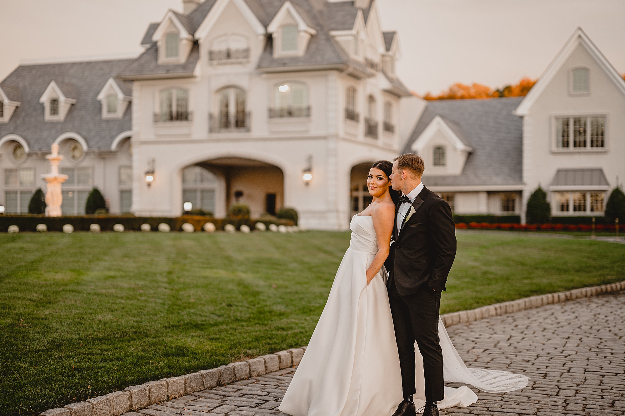 bride and groom hold hands while groom kisses bride's cheek in front of Park Chateau Estate 