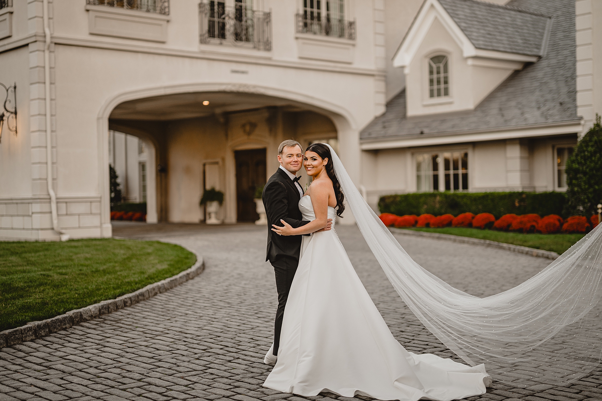 bride and groom hug with bride's veil floating behind them in front of Park Chateau Estate 
