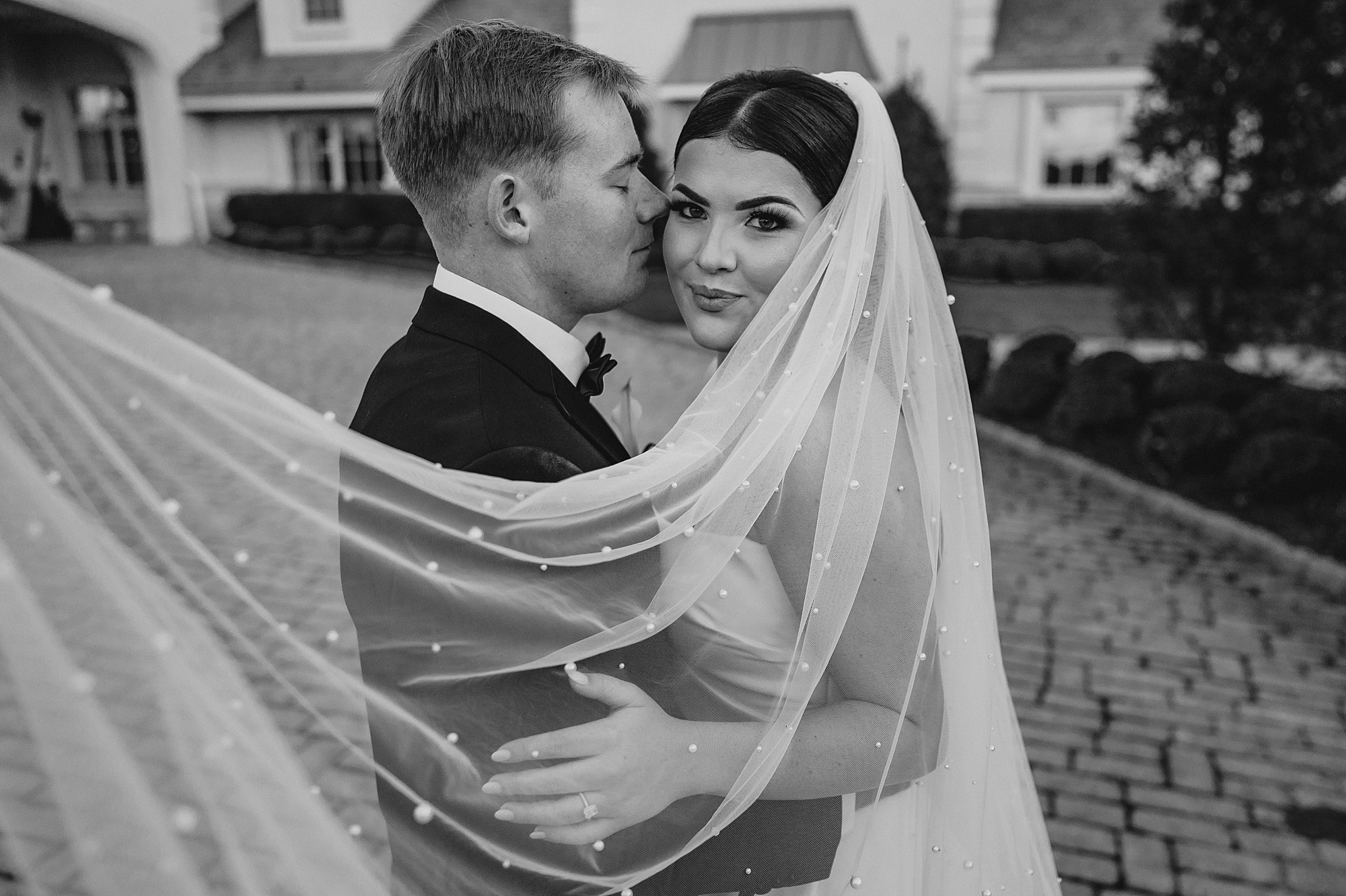groom hugs bride to him with veil wrapped around them both in NJ