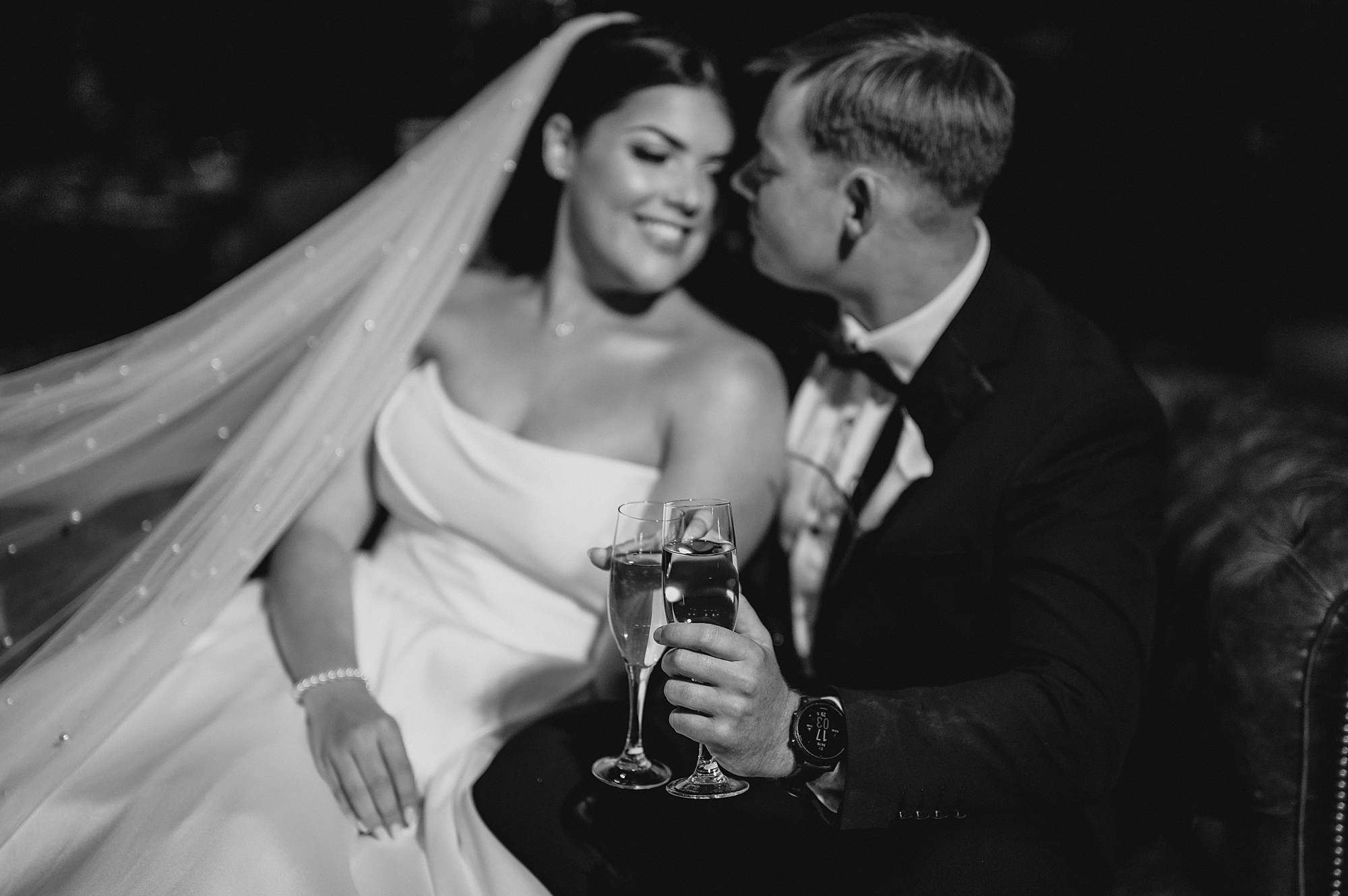 newlyweds hug on leather couch toasting glasses of wine at Park Chateau