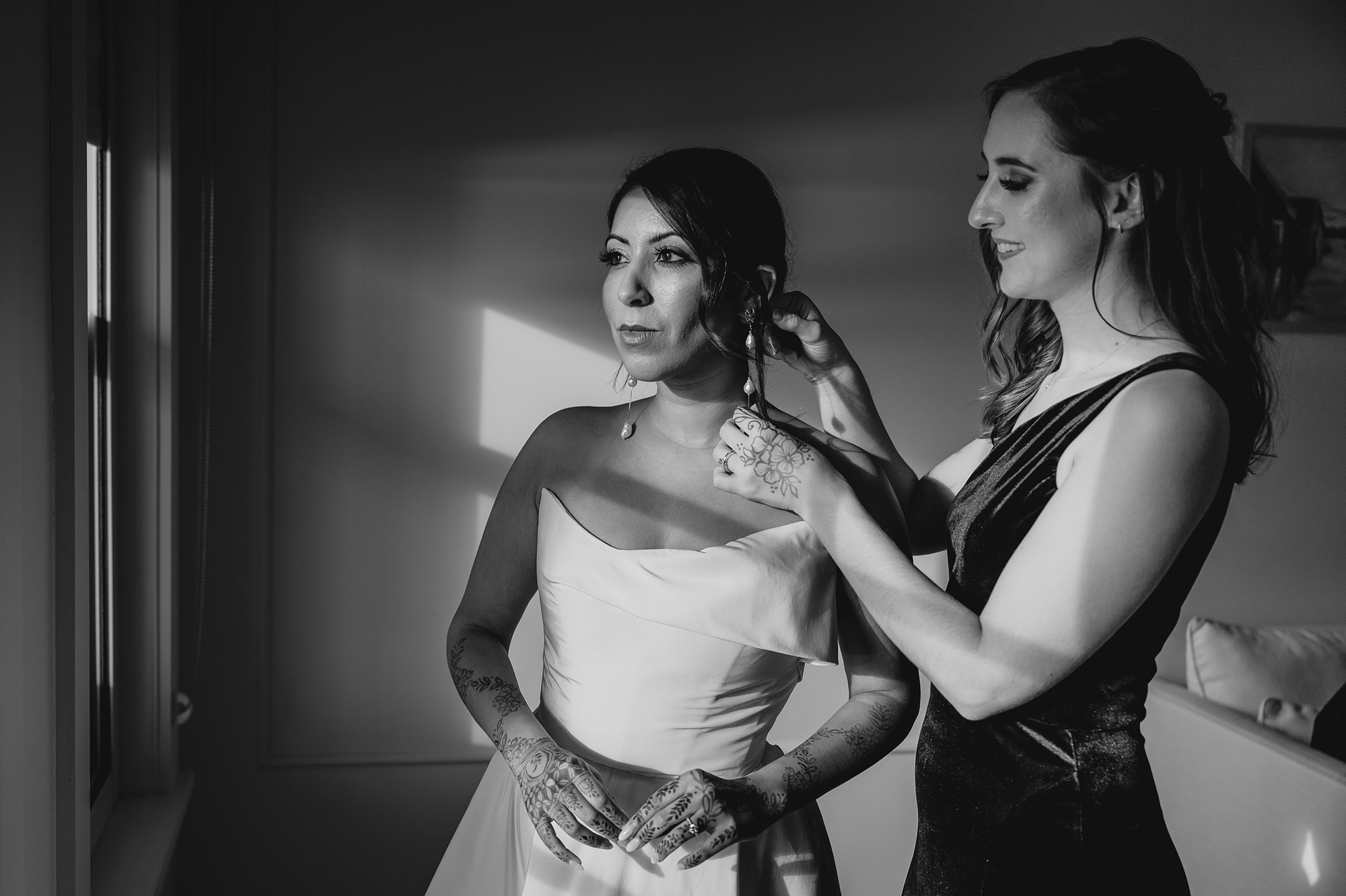 bridesmaid helps bride with dangling earrings on wedding day