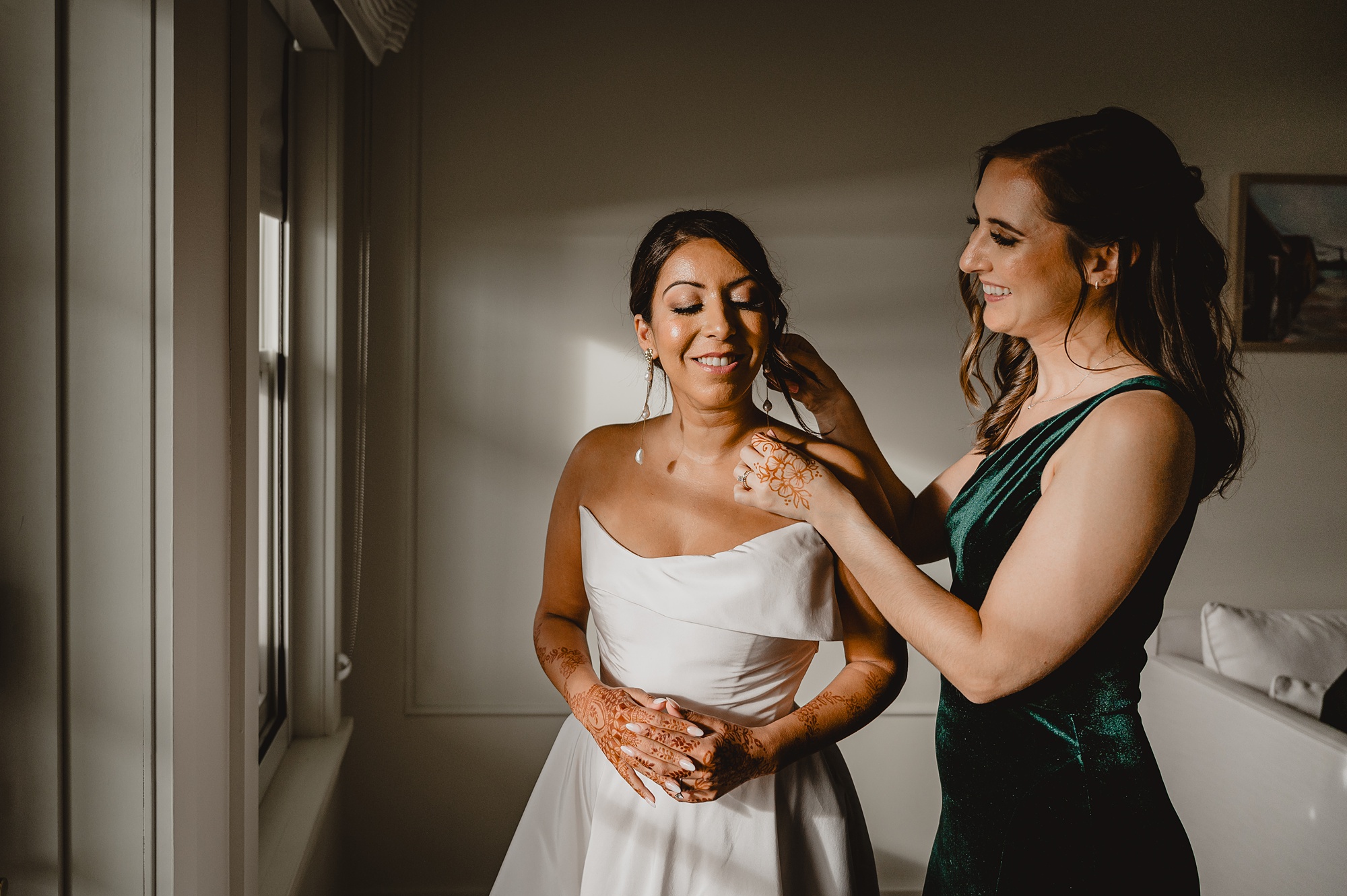 bridesmaids in green dress helps bride with earrings 