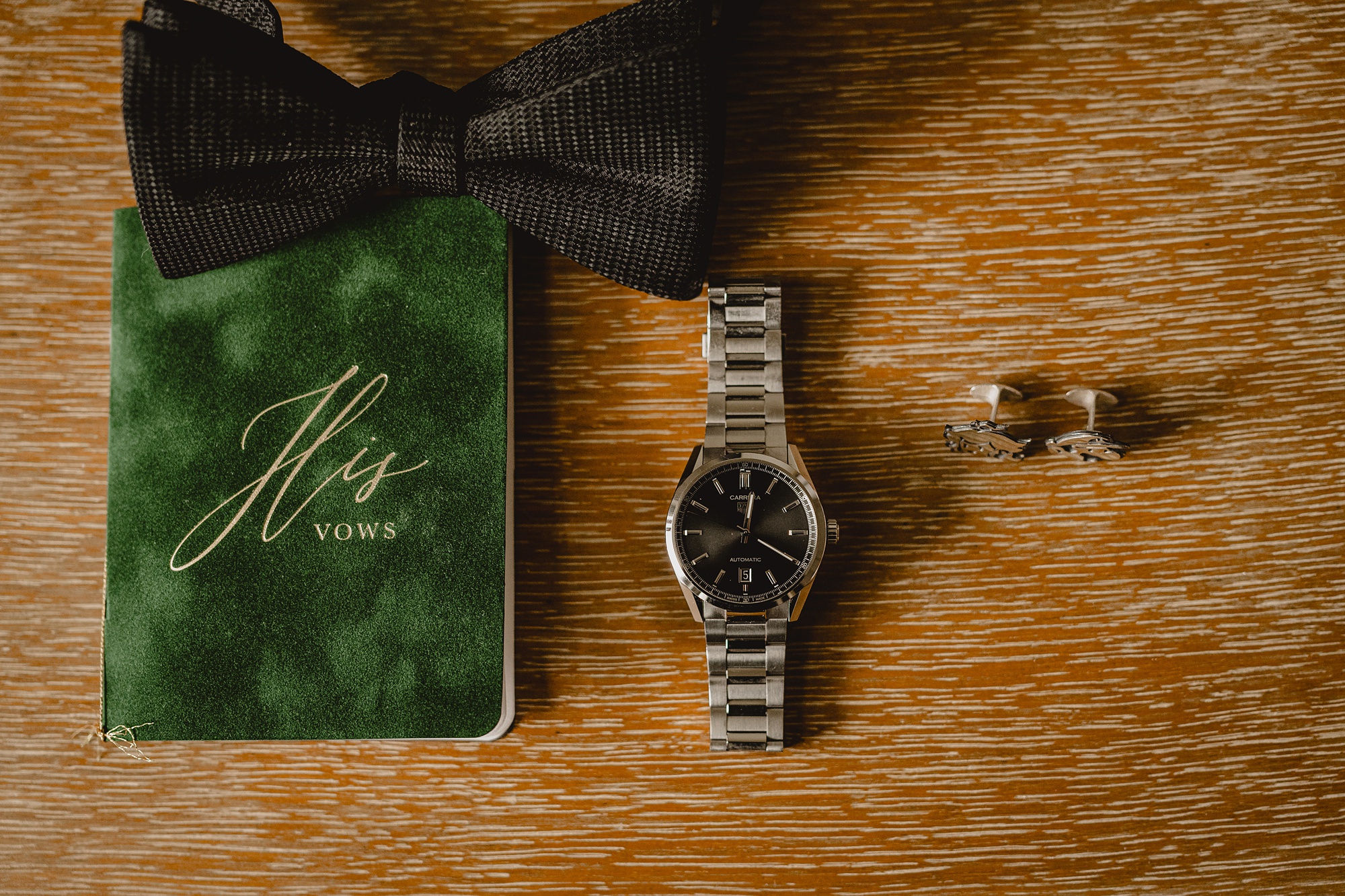 groom's watch, vow booklet and tie sit on wooden table