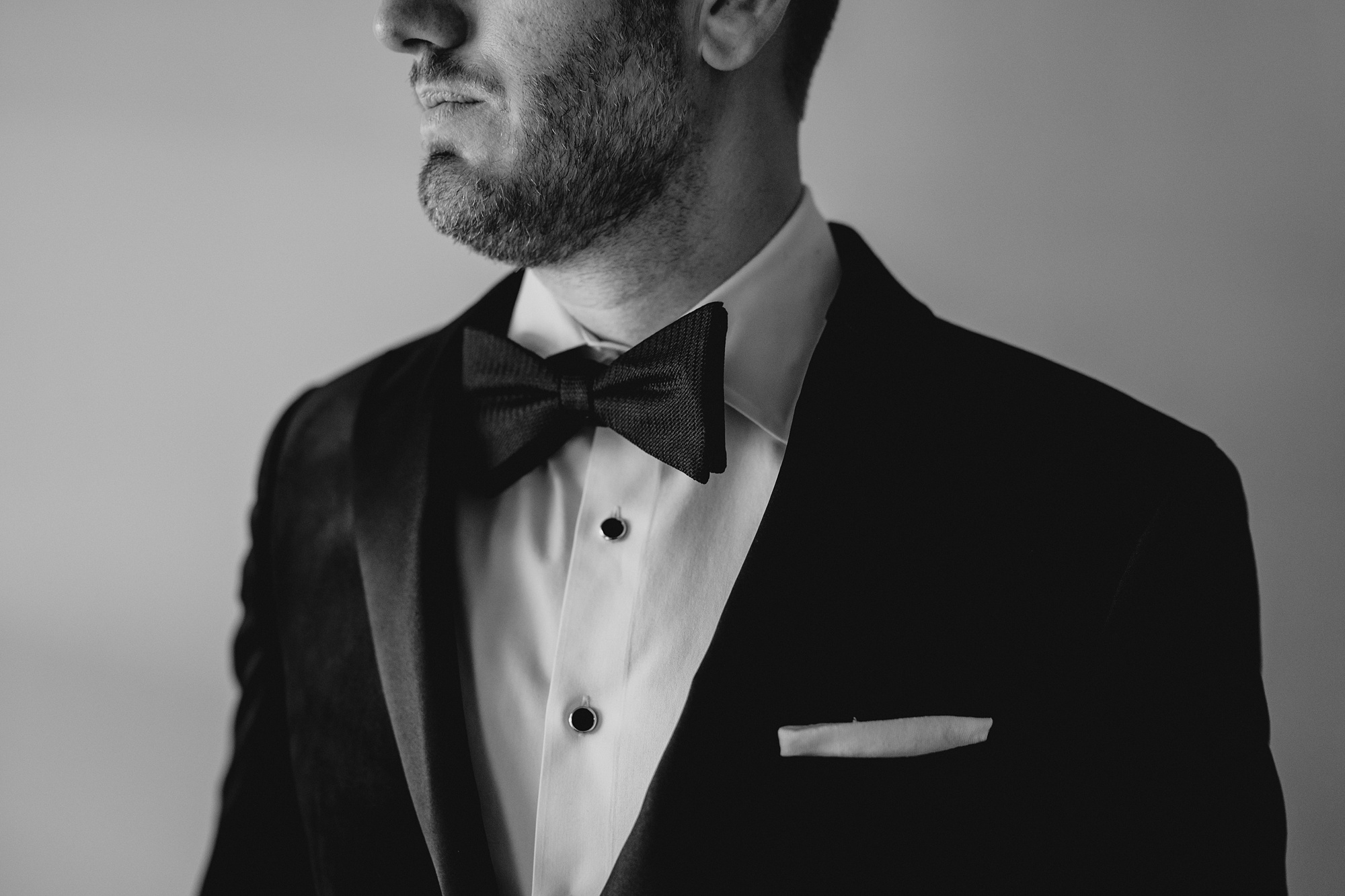 groom looks out window in black tie with bowtie 