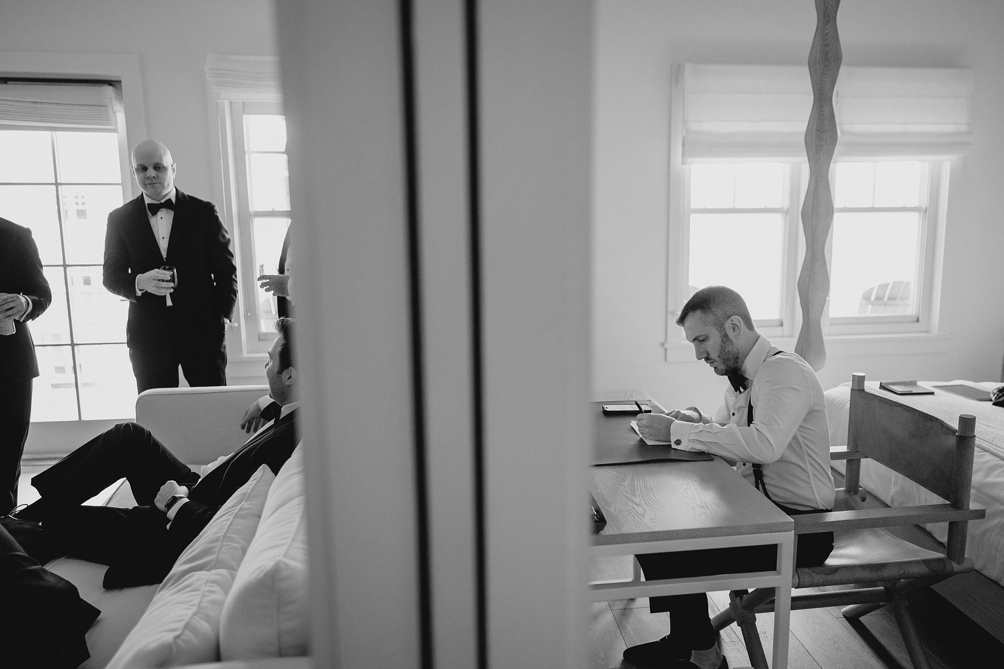 groom sits a hotel desk writing a letter to bride