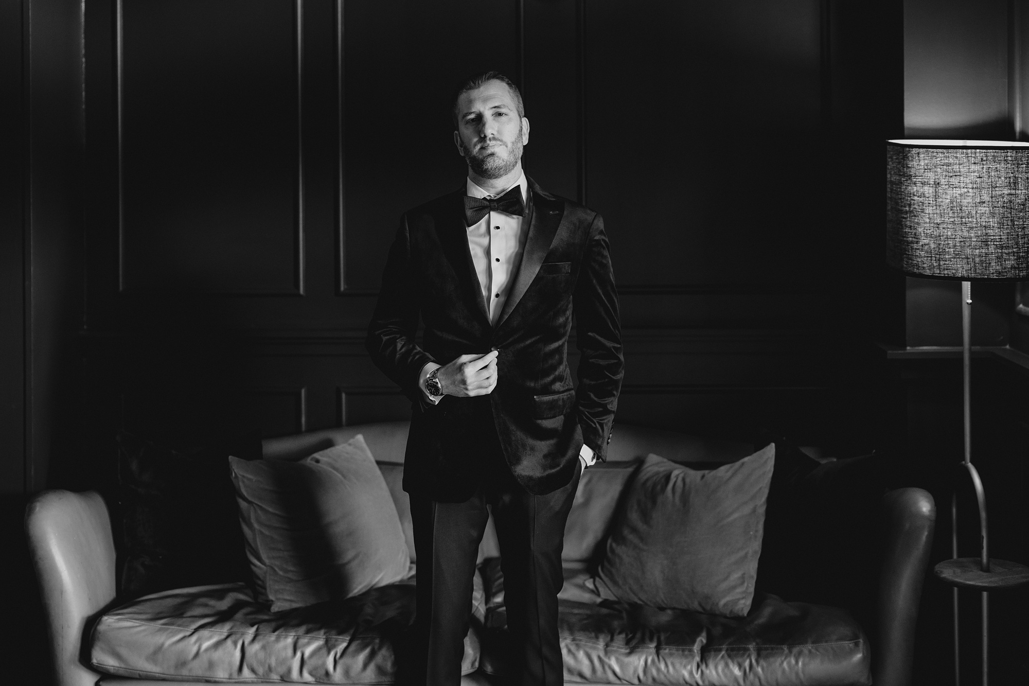 groom stands in front of couch of the blue room at the Lake House at Canandaigua