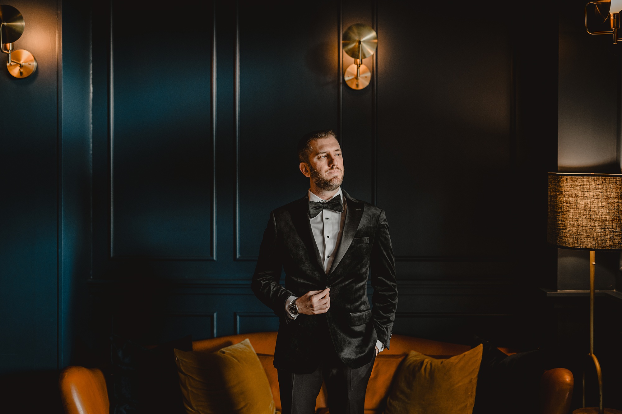 groom stands in front of leather couch at the Lake House at Canandaigua