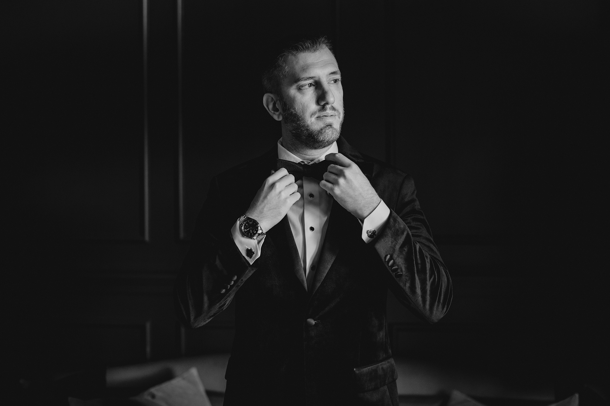 groom adjusts bowtie standing in library at the Lake House at Canandaigua