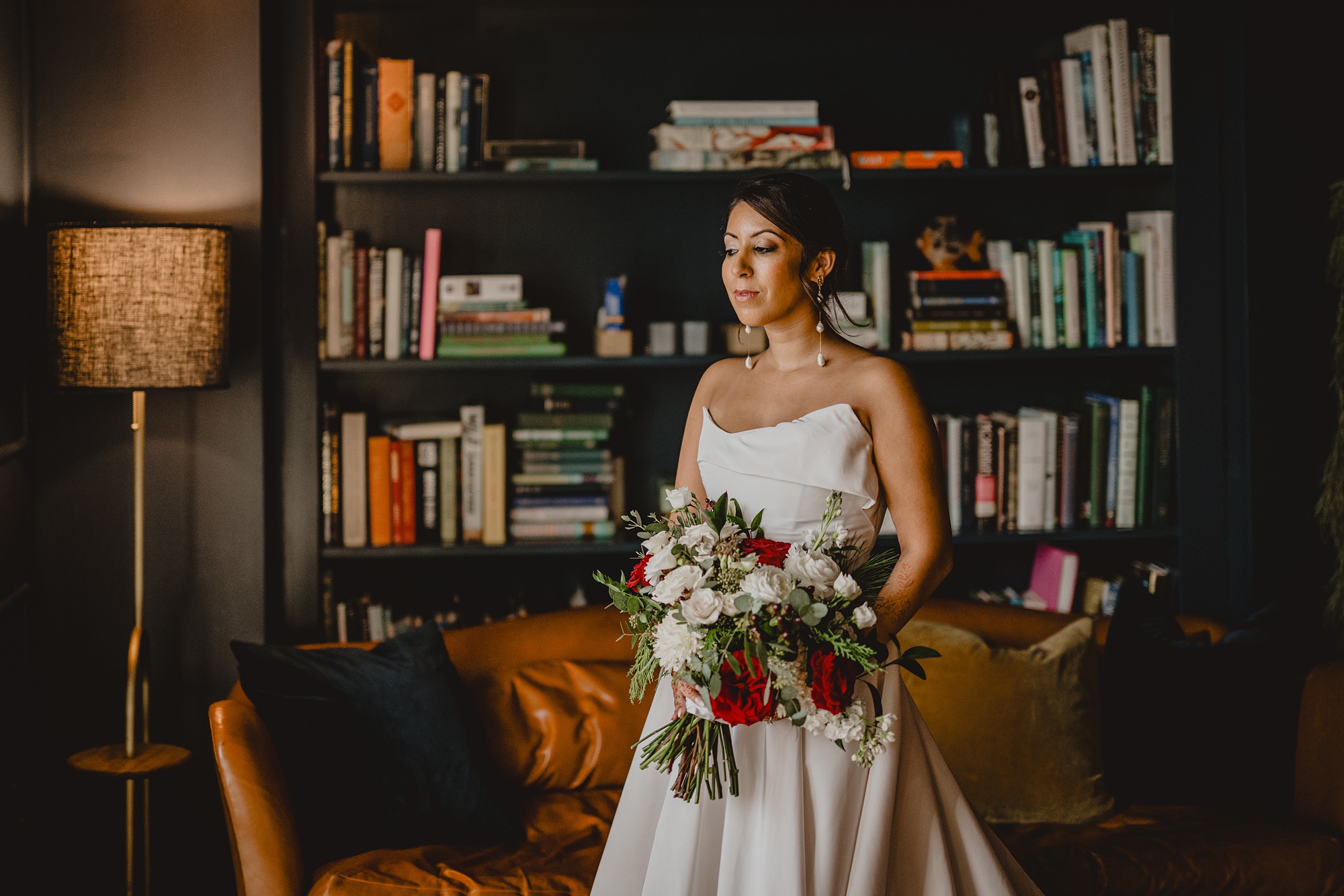 bride stands in strapless gown holding bouquet of white and red flowers 