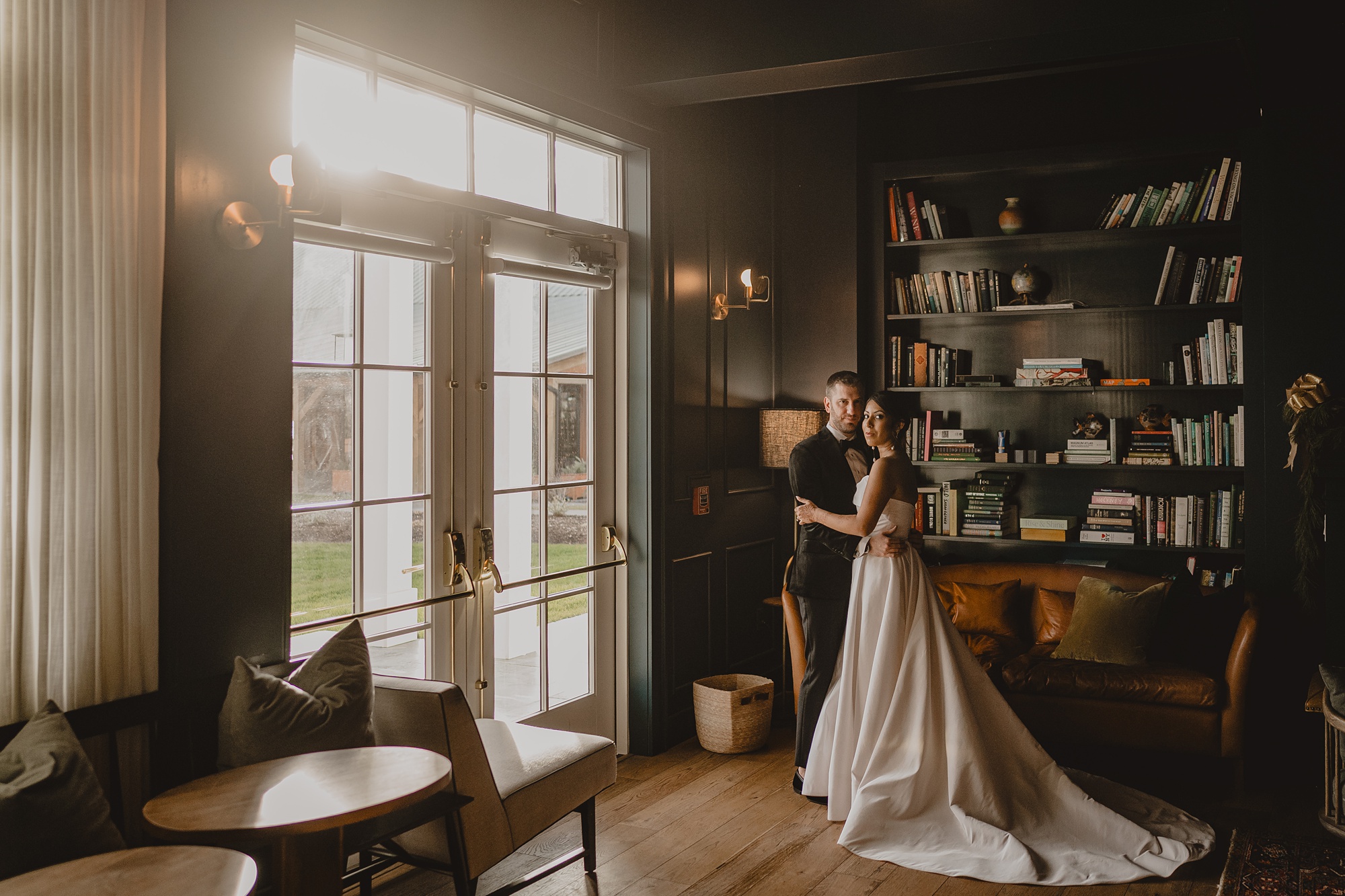bride and groom stand in front of window in the library at the Lake House at Canandaigua