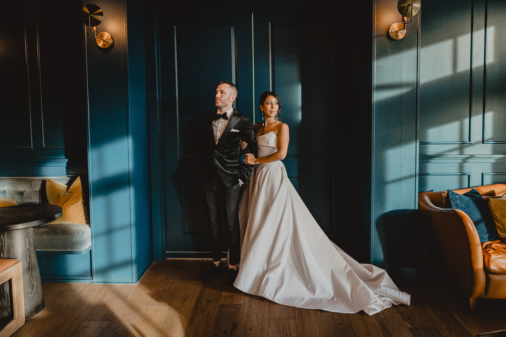 bride holds groom's arm looking away from him by wooden doors at the Lake House at Canandaigua