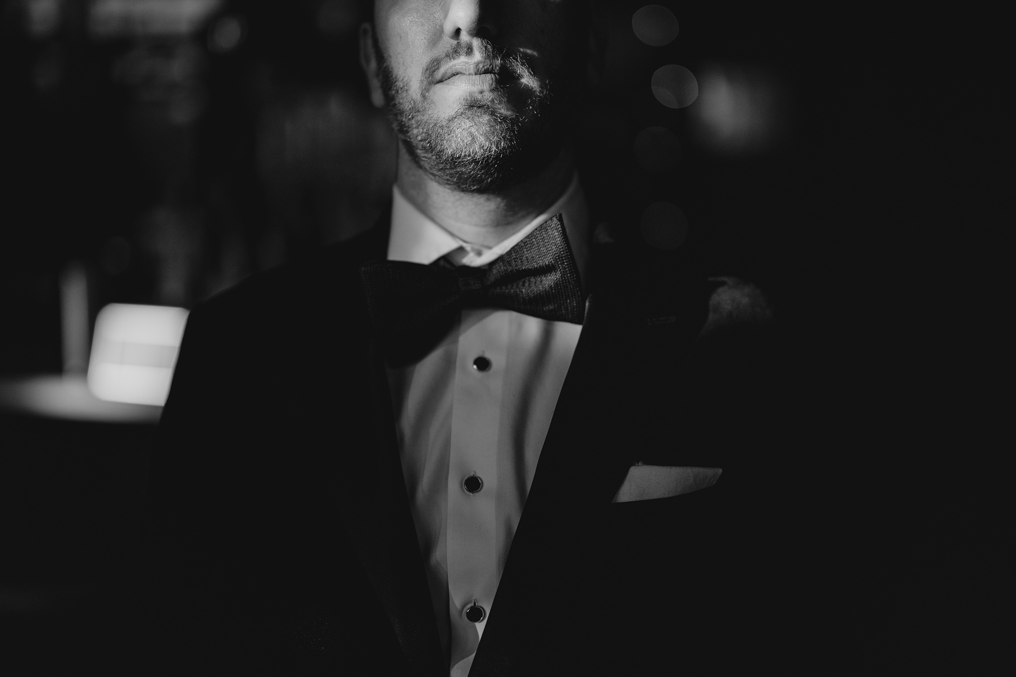groom stands in black tux with black bowtie 