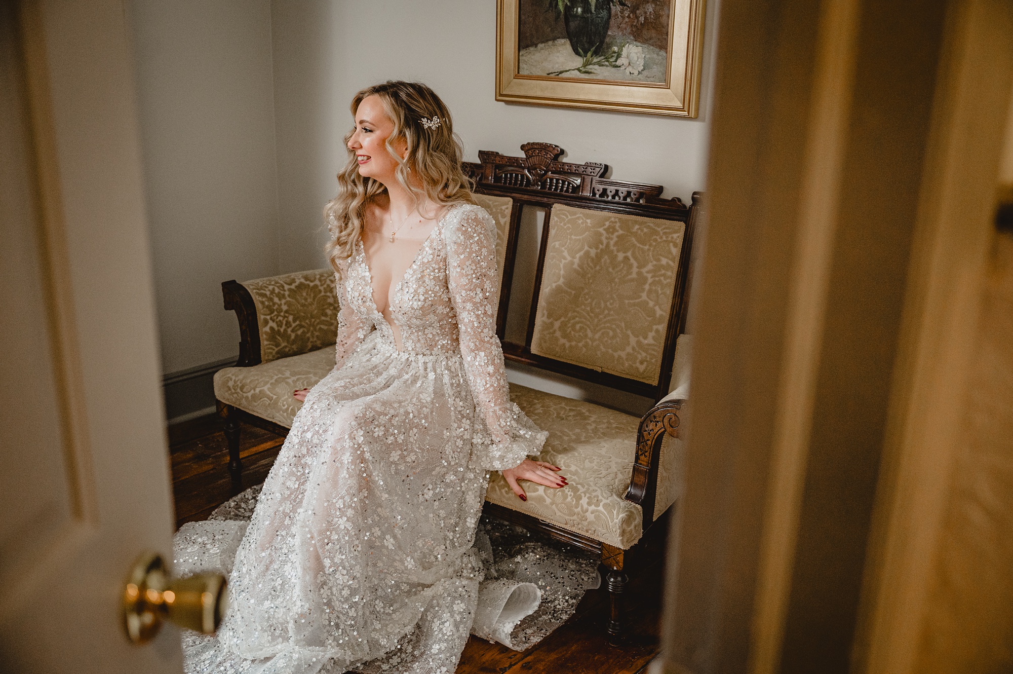 bride sits on gold and wooden chair in long sleeve wedding gown