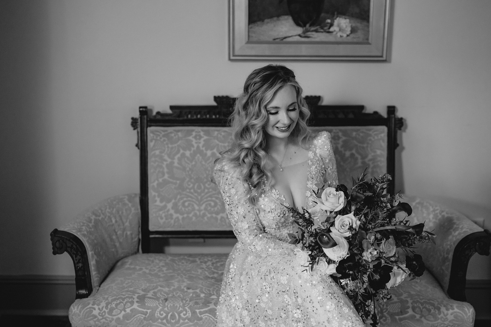 bride looks down at cascading bouquet sitting on vintage chair