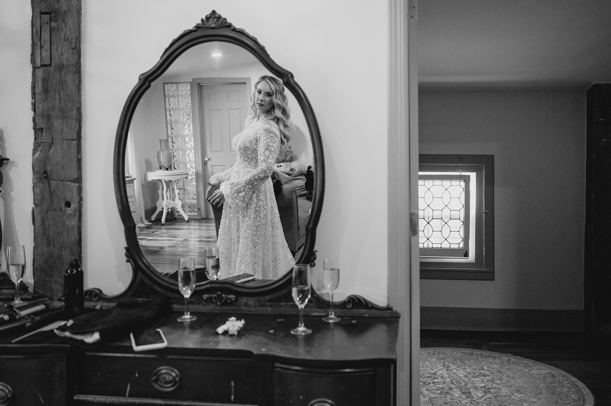 bride looks at back of dress in mirror above vanity in bridal suite