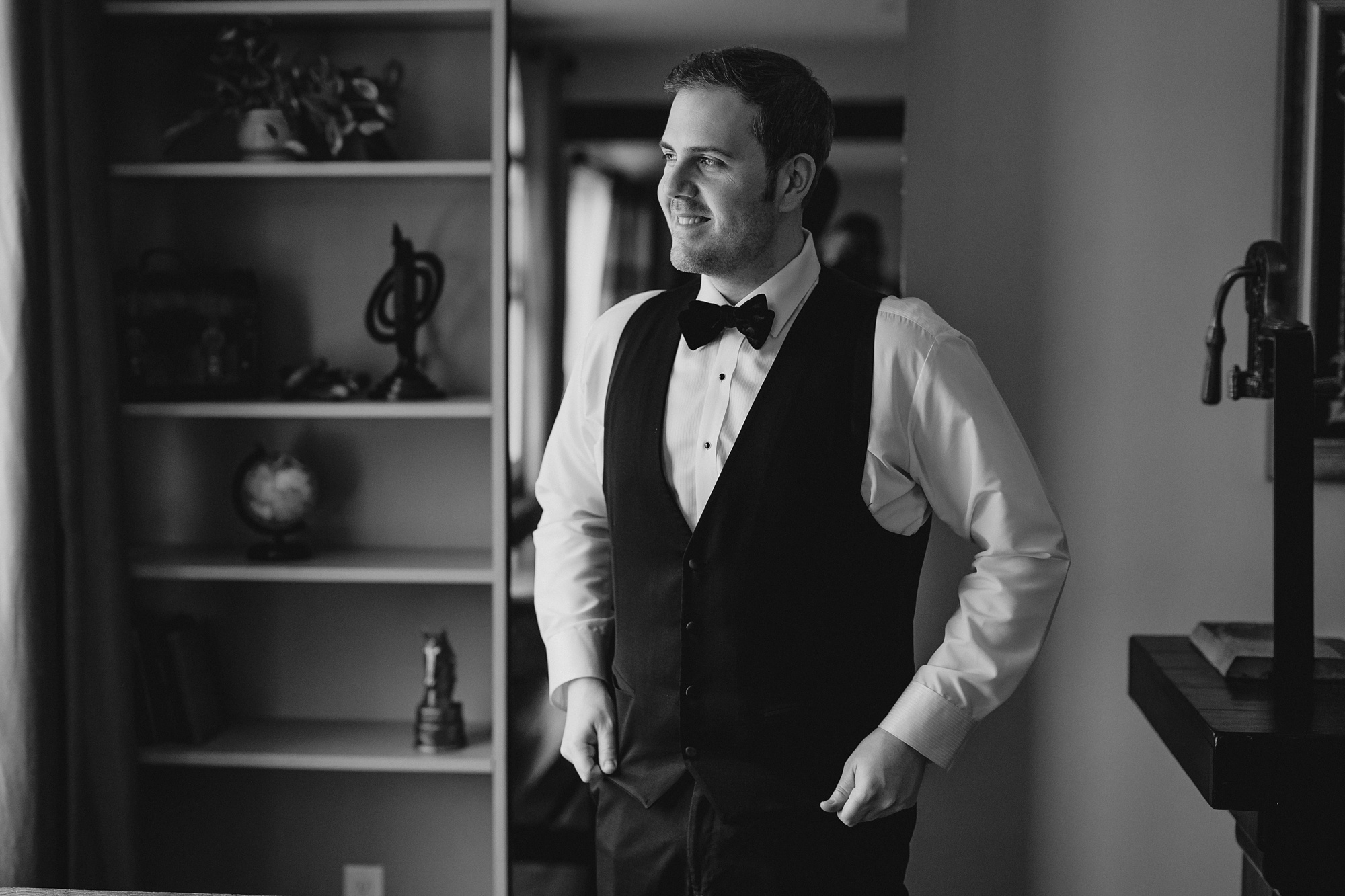 groom stands adjusting vest in library at David's Country Inn