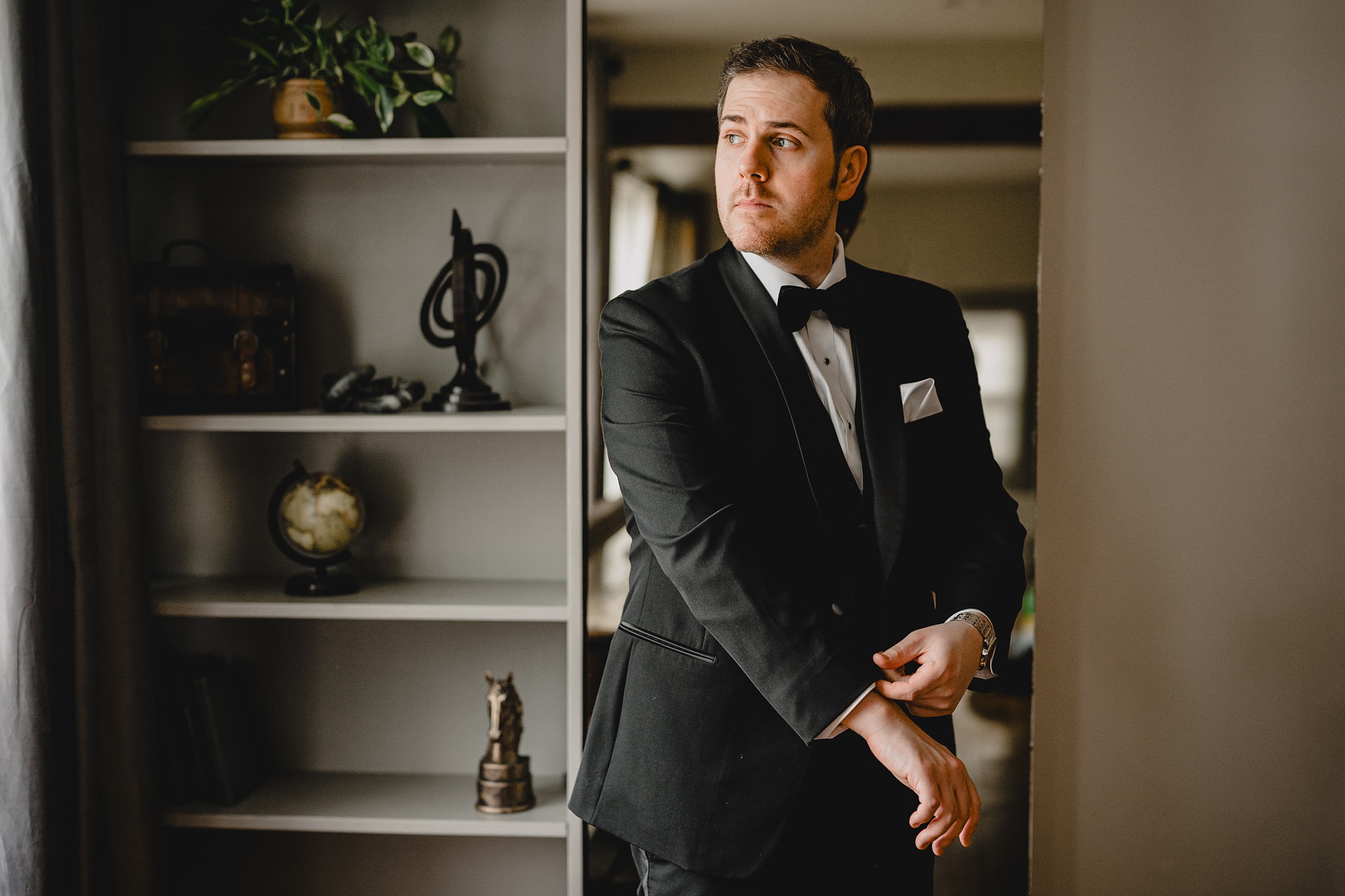 groom pulls on sleeves of black suit inside library at David's Country Inn