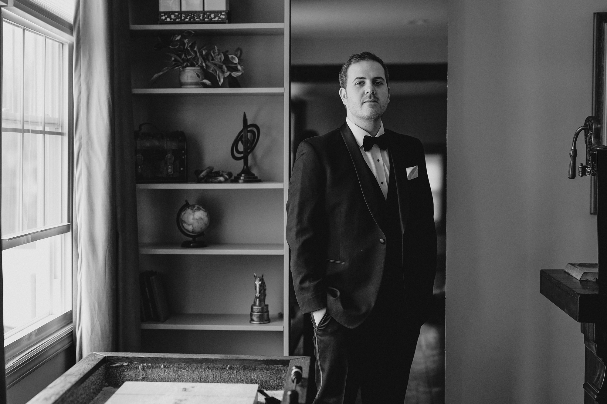 groom stands with his hands in pockets of jacket