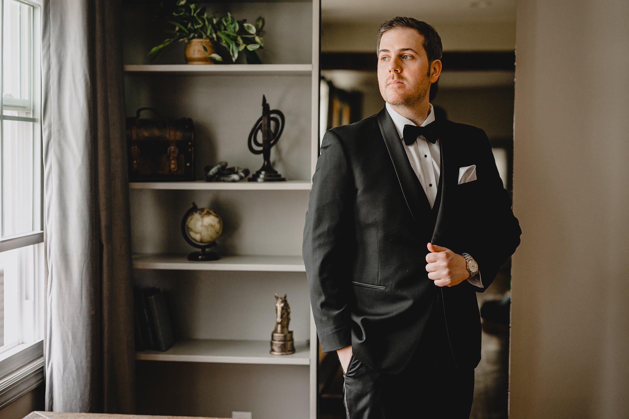 groom holds lapel of his black suit by library shelves