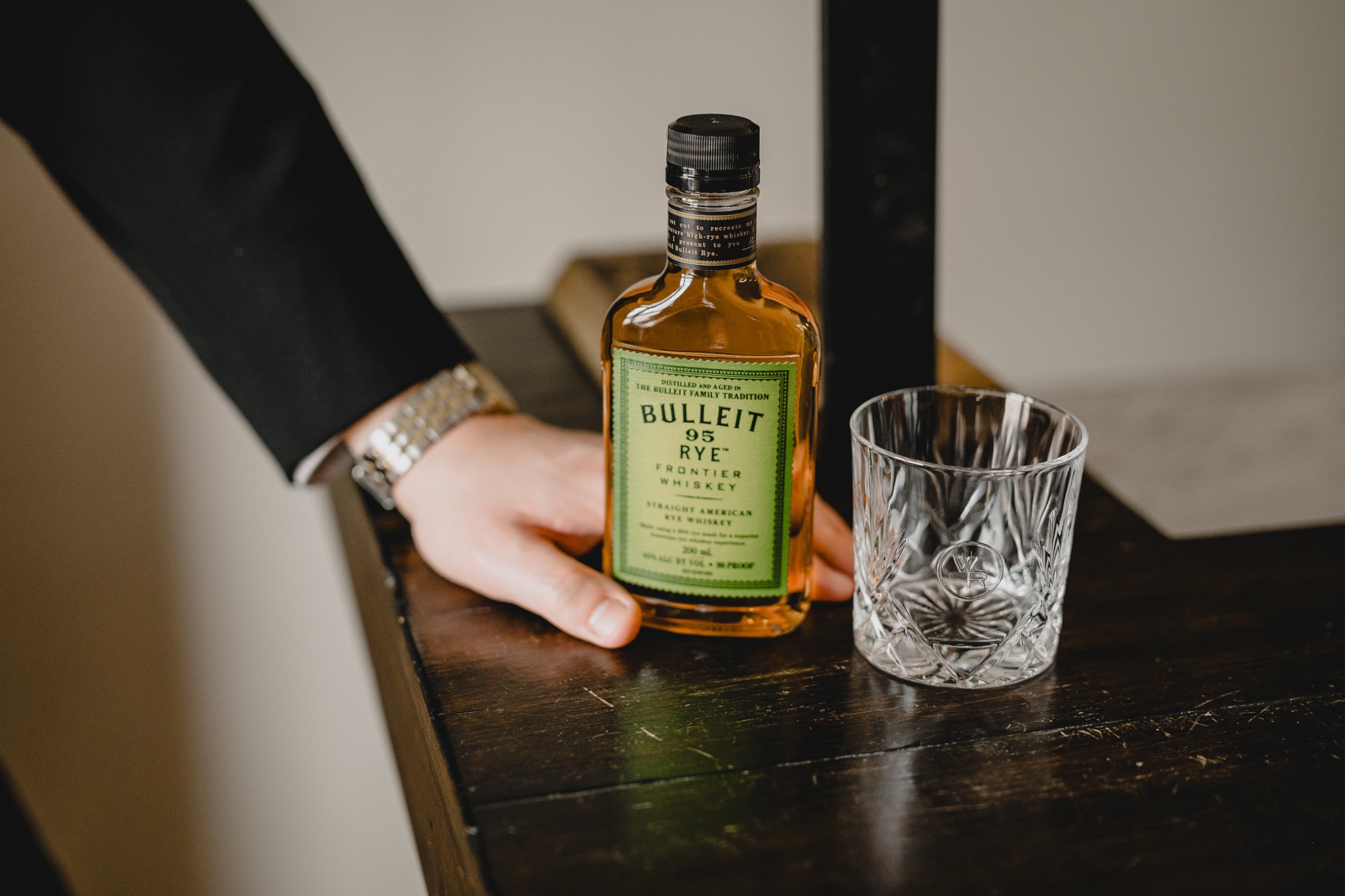 groom puts hand on bottle of alcohol by glass