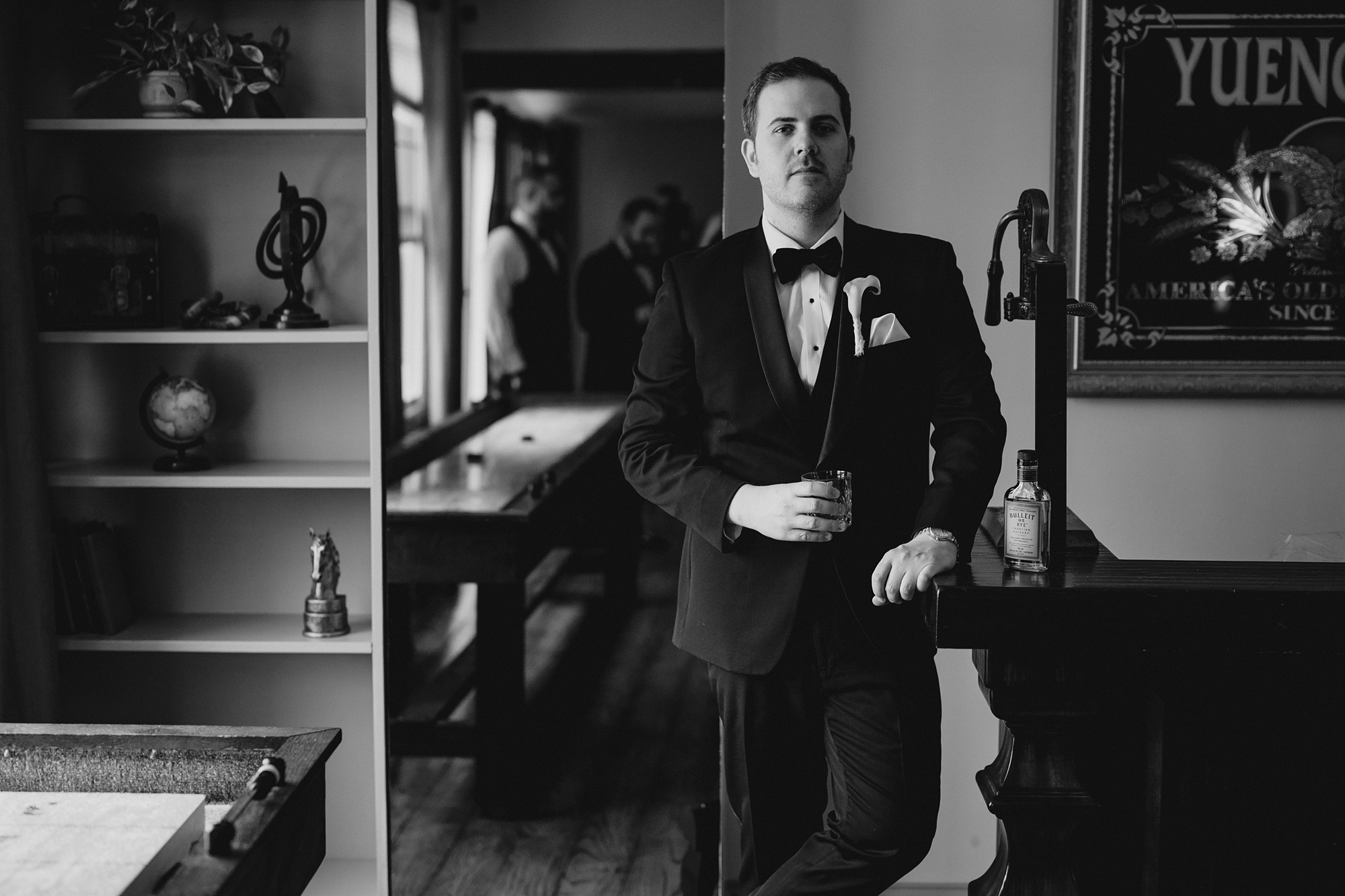groom leans on table with a drink in his hand at David's Country Inn