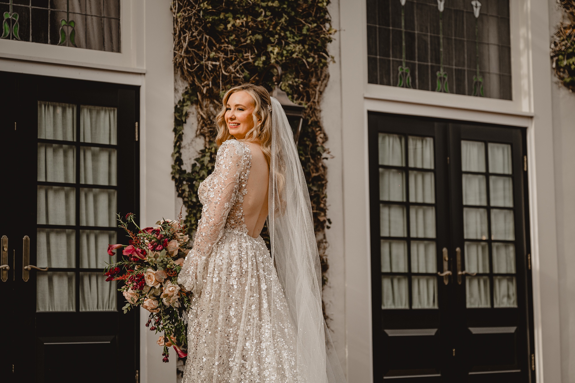 bride looks over shoulder holding red and white flowers on brick patio at David's Country Inn