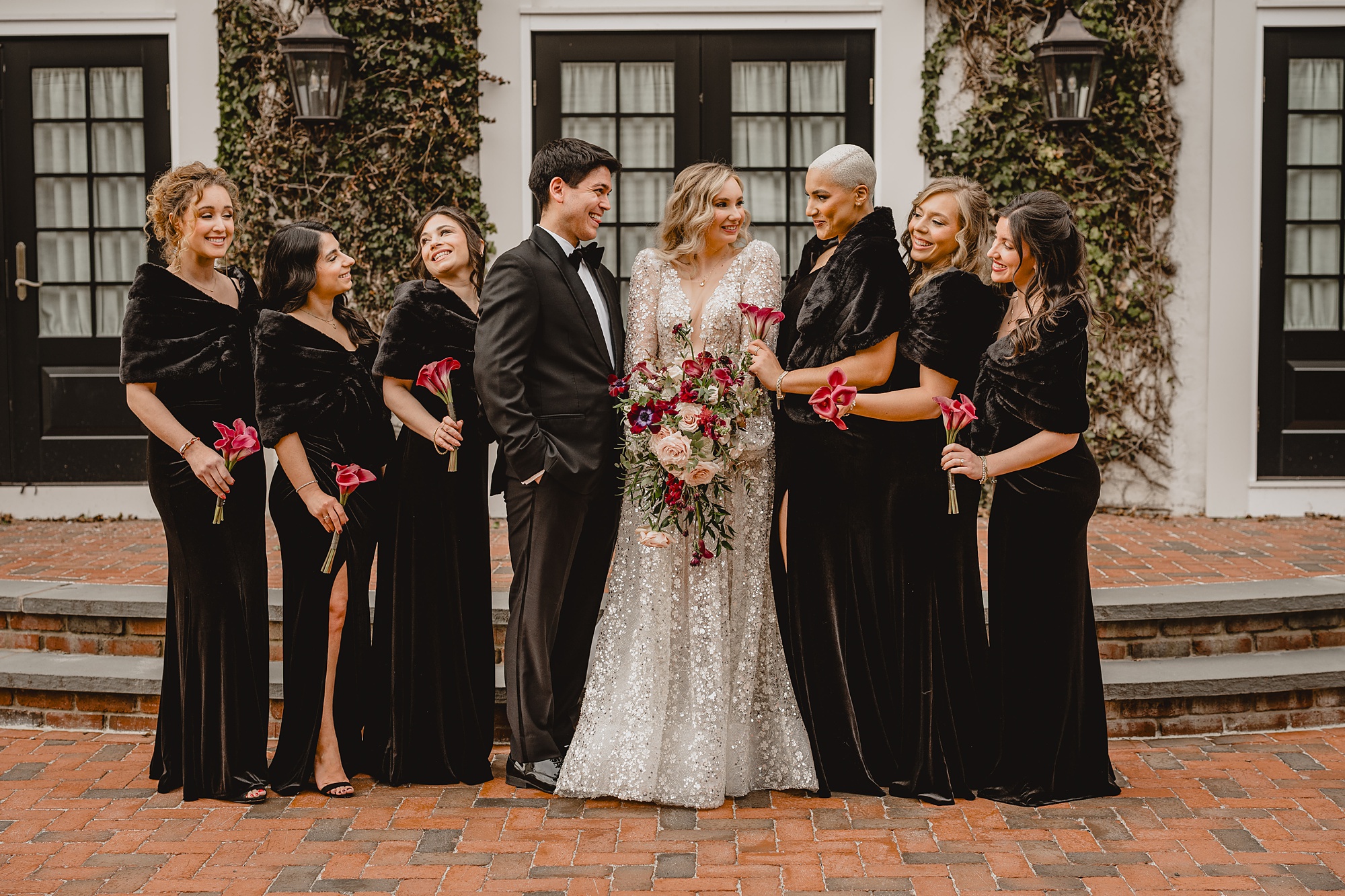 bride stands with bridal party in black dresses on brick patio