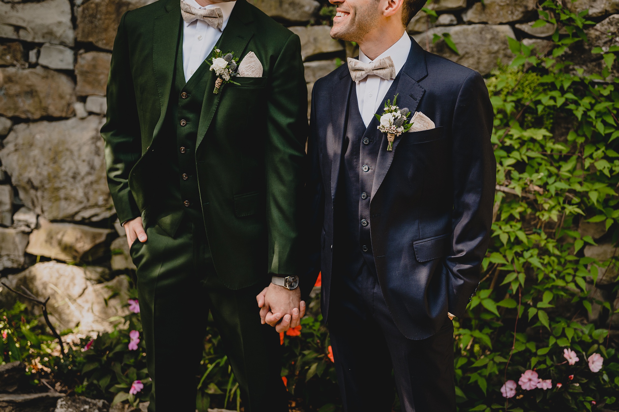 groom in emerald suit holds hands with groom in navy suit