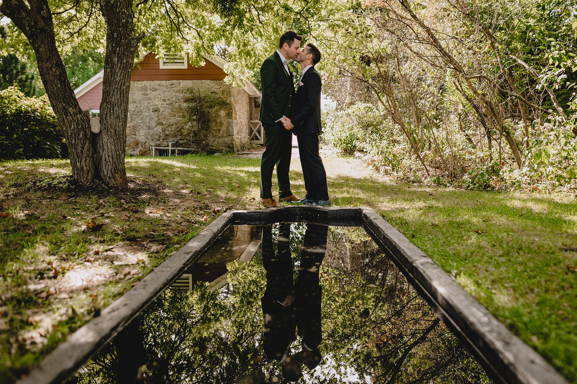 husbands kiss in front of reflection pool at Cross Keys Estate