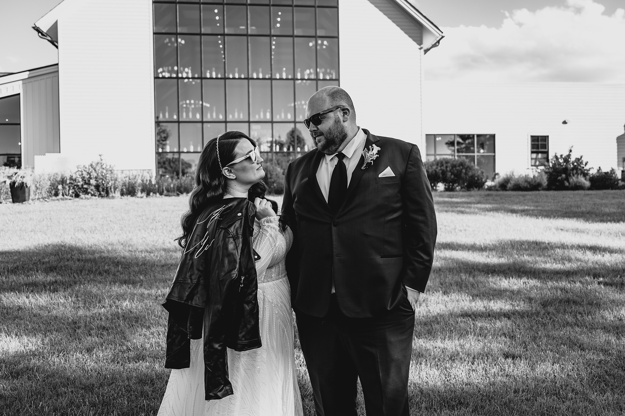 bride looks at groom with leather jacket over her shoulder outside Cross Keys Estate