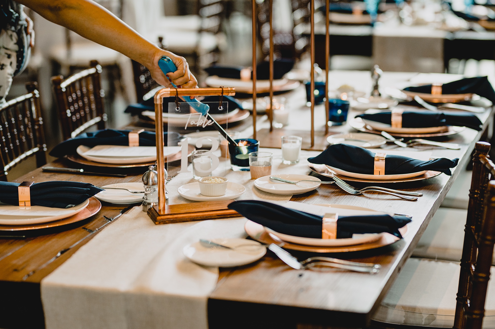 woman lights candle on reception table with blue and gold accents