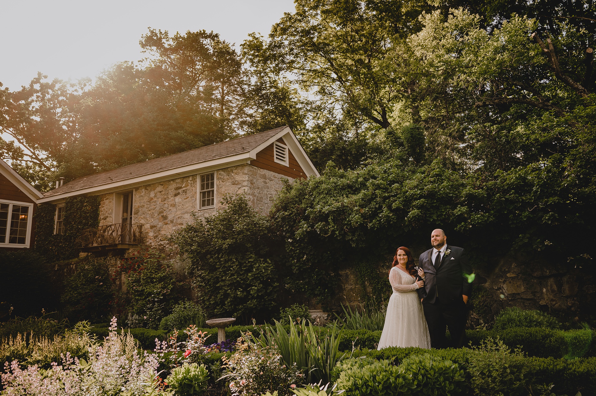 bride and groom stand in gardens in front of stone house at Crossed Keys Estate
