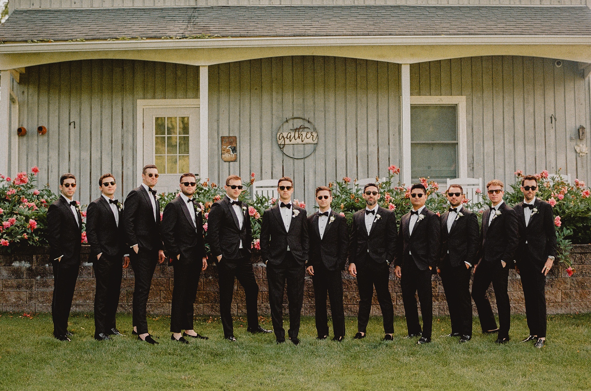 groom poses with groomsmen in front of farmhouse at Perona Farms