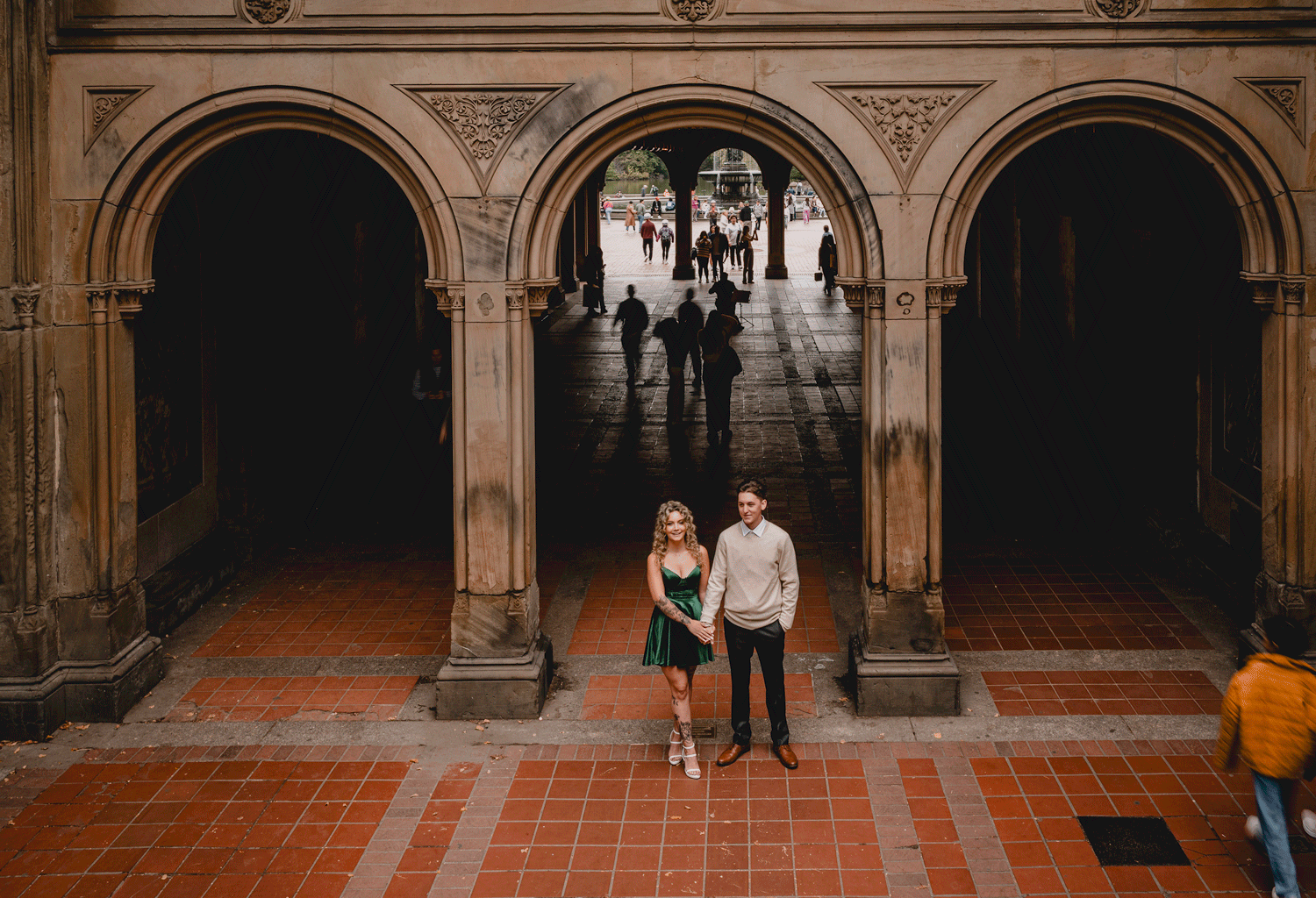 man and woman stand in Central Park arches while people mill around them