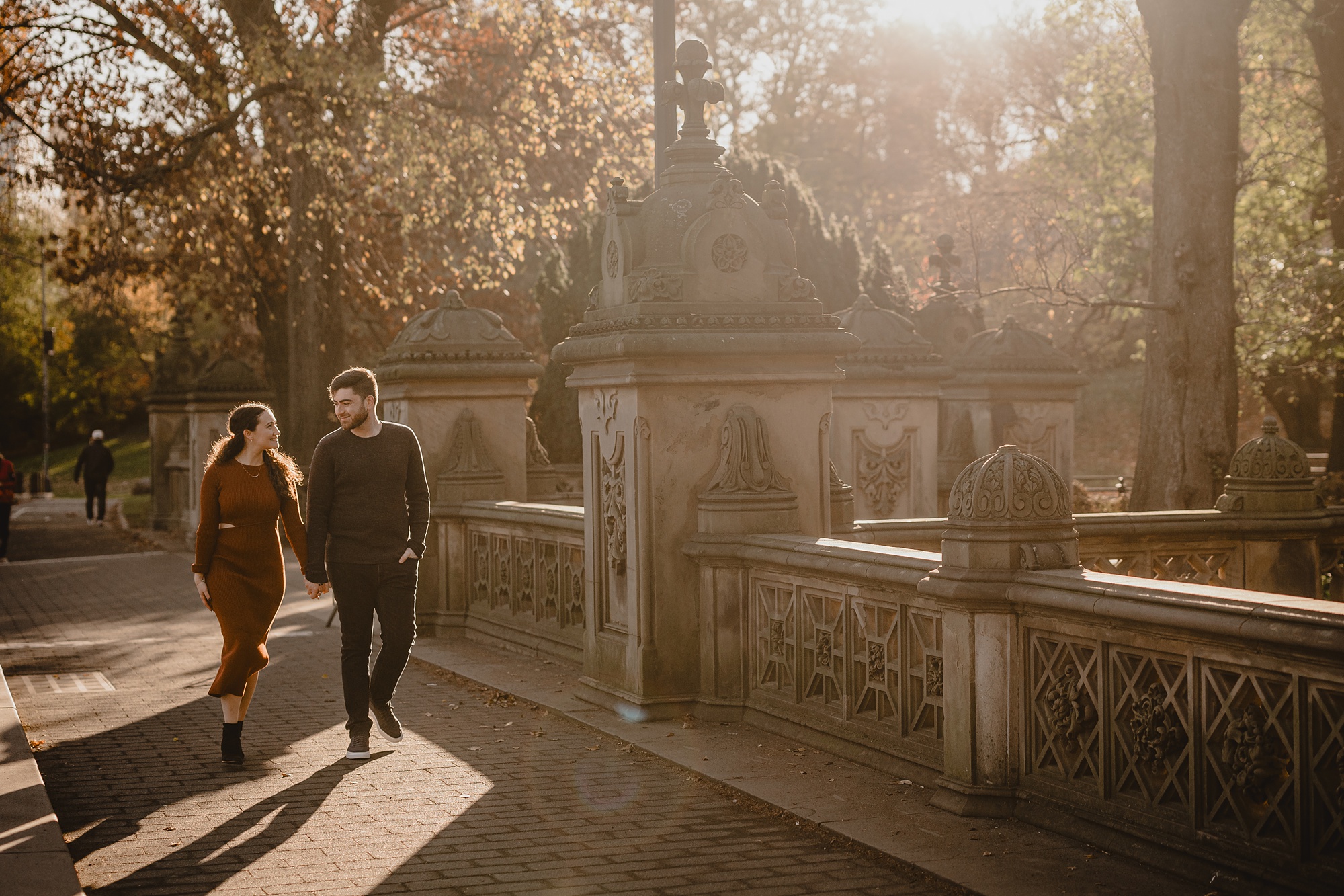 couple holds hands walking on Bow Bridge in Central Park