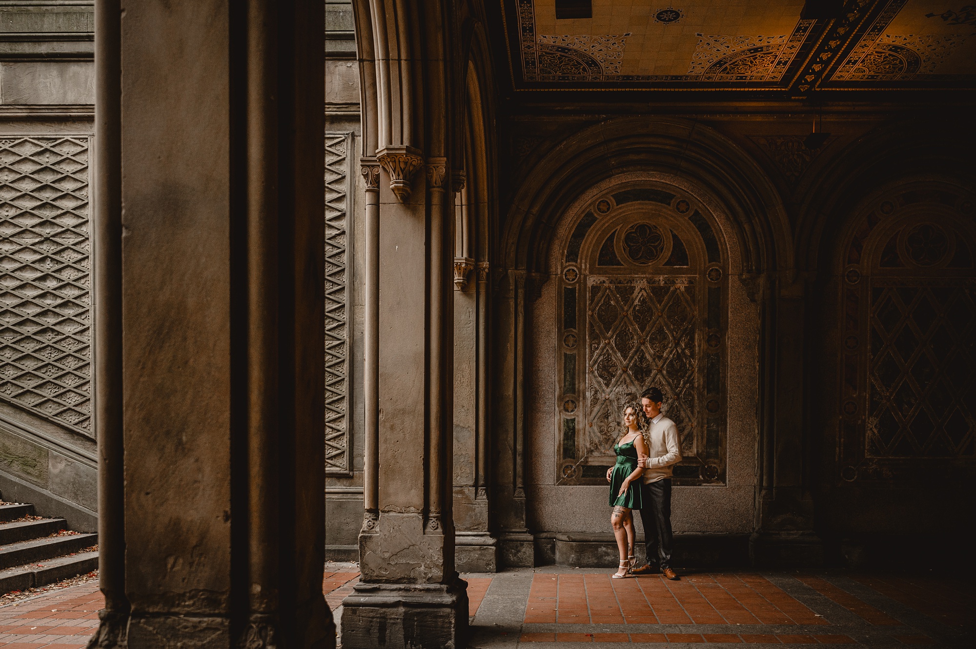 engaged couple hugs by mosaic in Central Park staircase