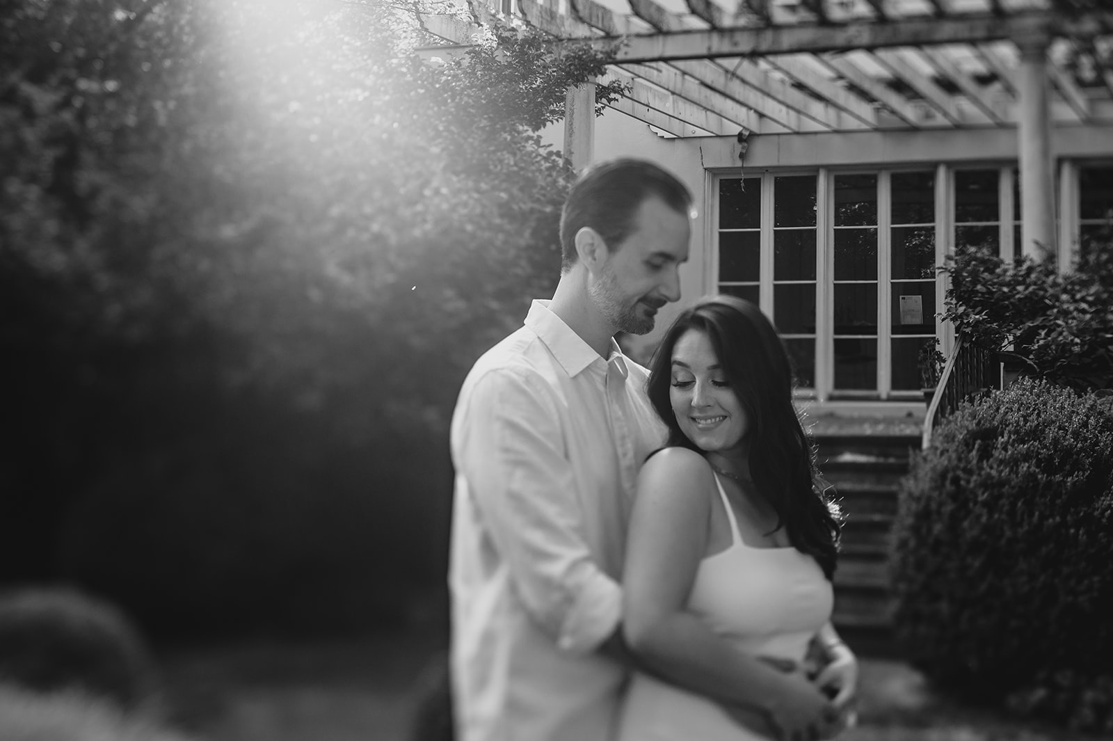 man hugs woman around back in front of wooden arbor over window