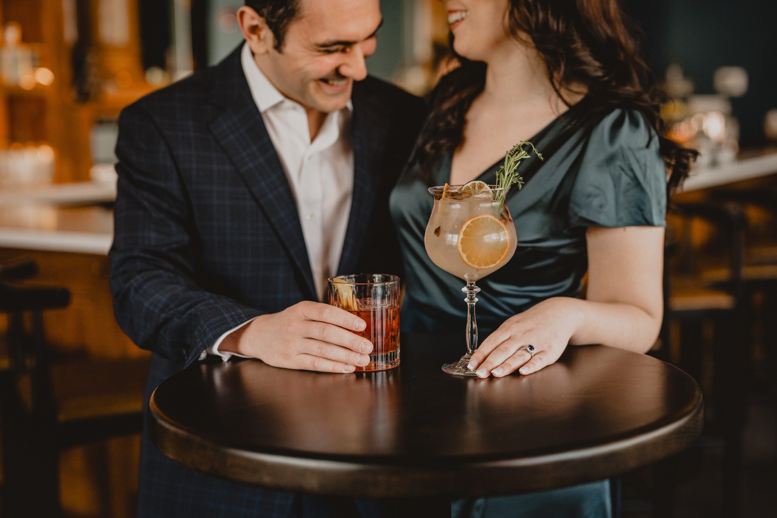 man and woman sit holding drinks during summer engagement session