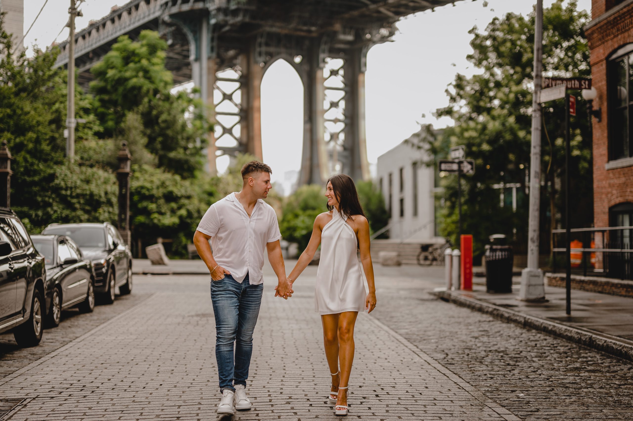 man and woman hold hand walking away from bridge in DUMBO