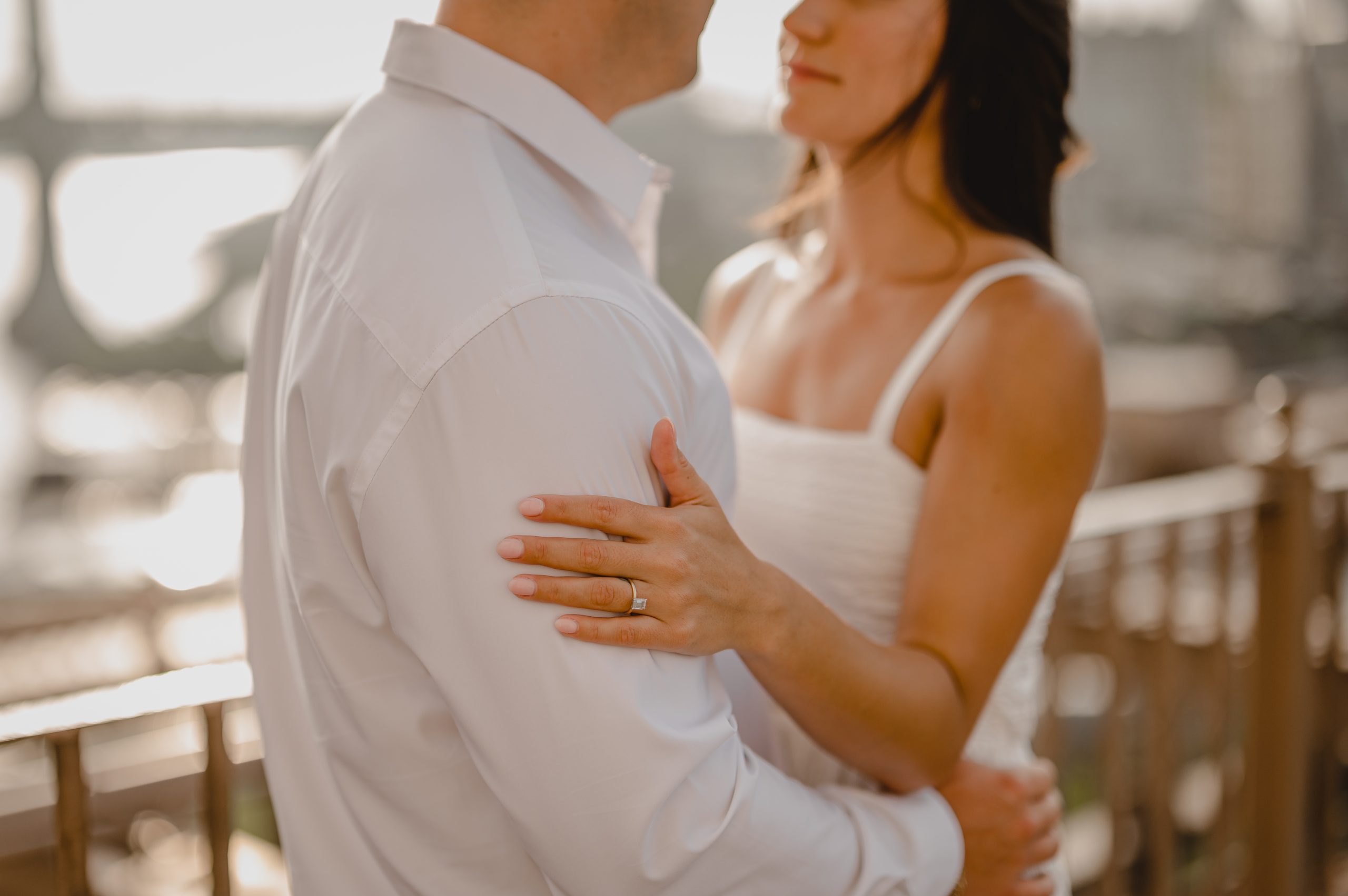 woman in white dress holds man's arm in white shirt showing off engagement ring