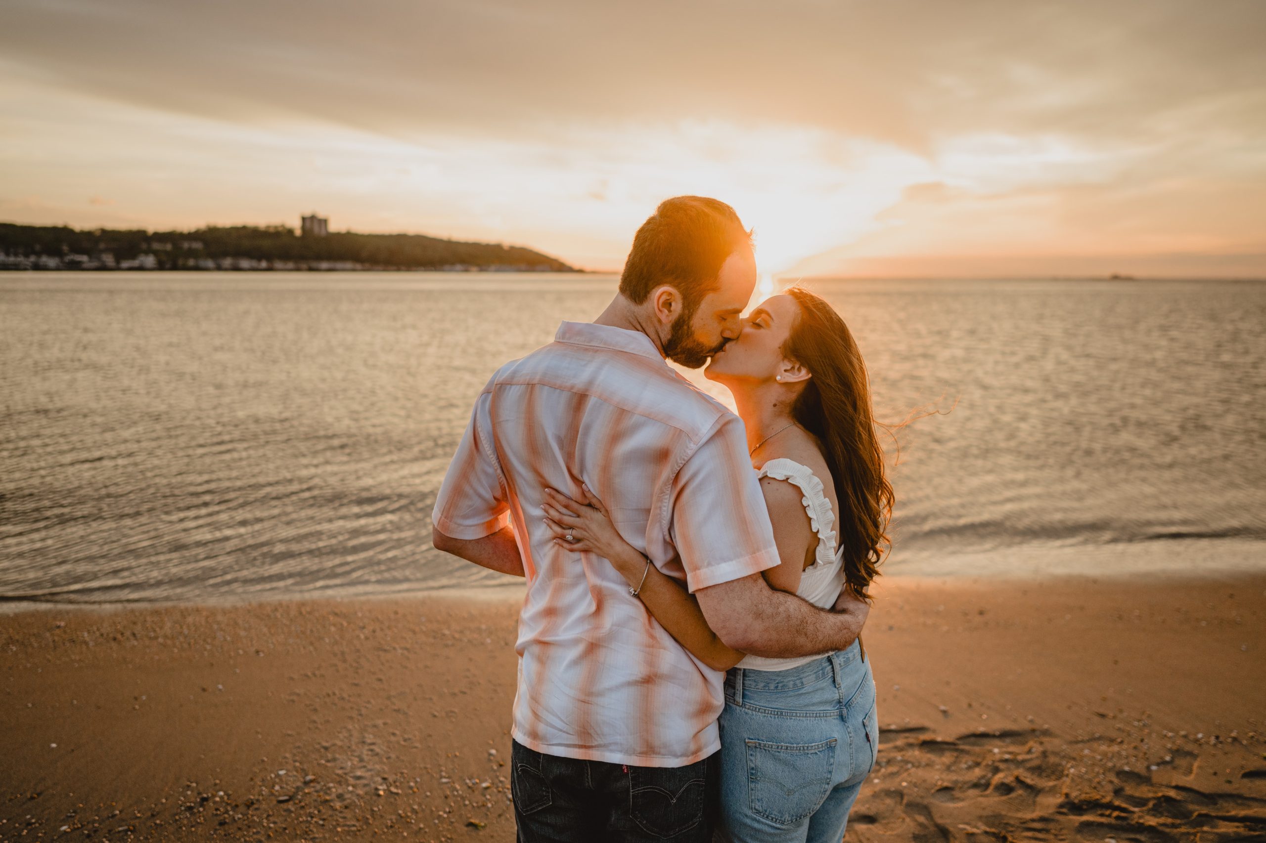 engaged couple kisses on beach at sunset during summer engagement session