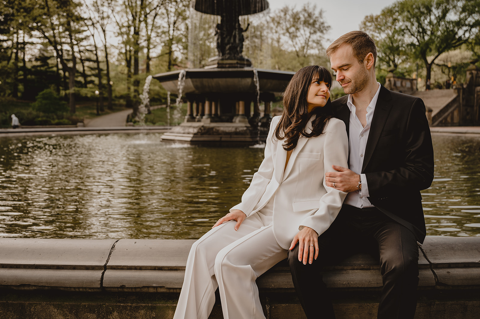 woman sits next to man leaning on him on edge of Bethesda Fountain