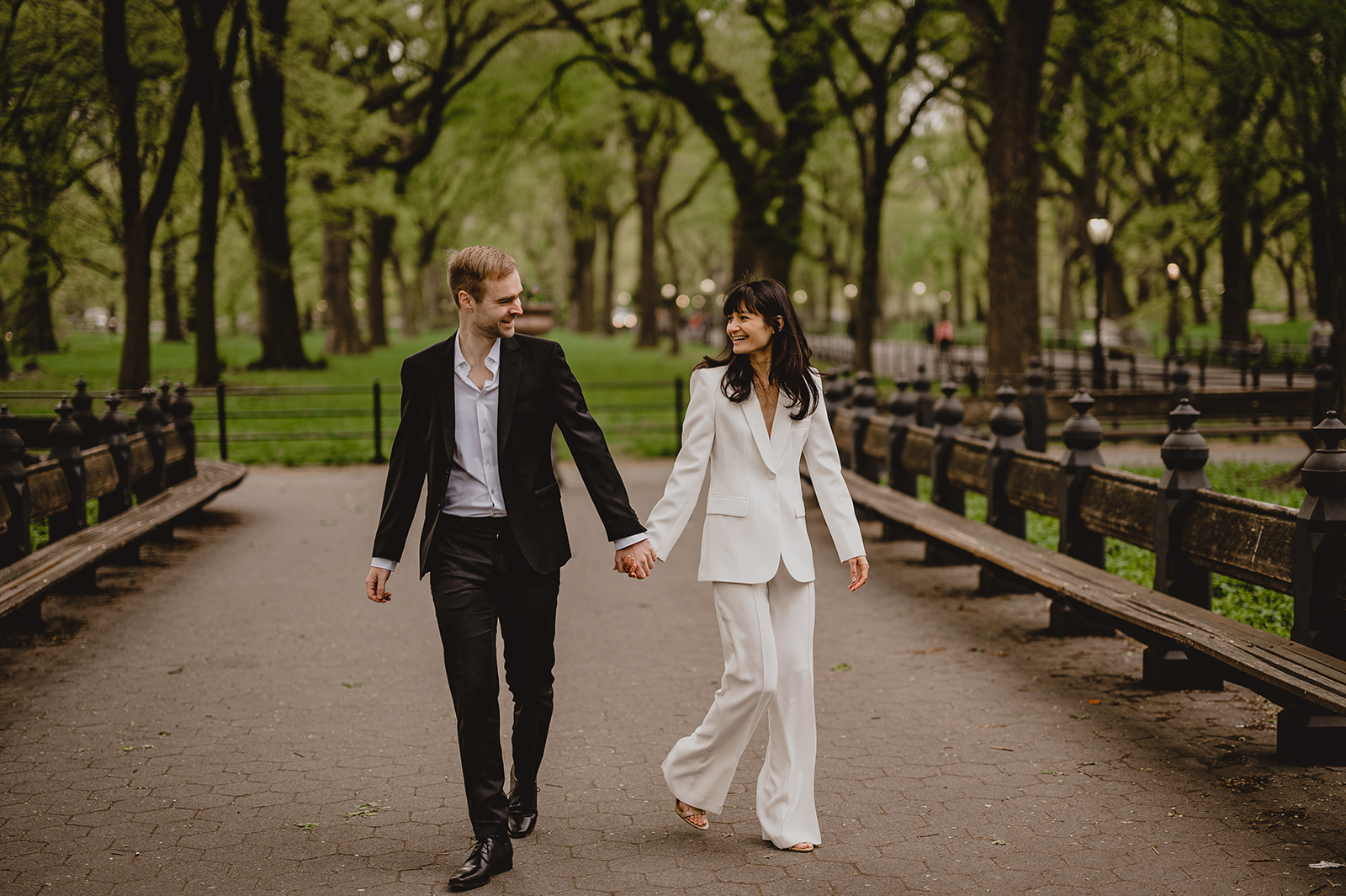 couple holds hands walking down path inside Central Park
